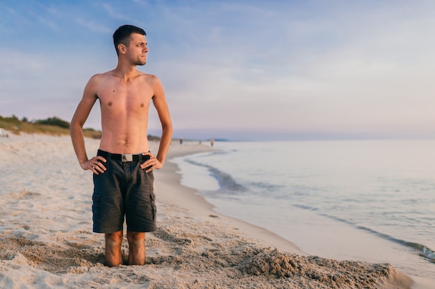 Młody człowiek stojący w dziurze na plaży