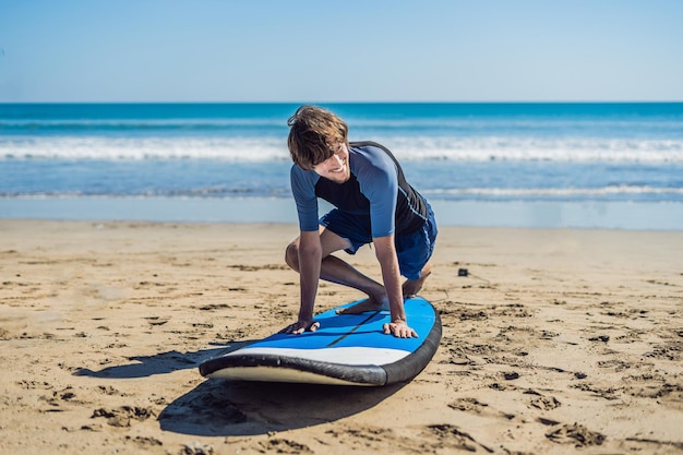 Młody człowiek szkolenia surfer przed pójściem do składu na piaszczystej plaży. Nauka surfowania. Koncepcja wakacji. Wakacje. Turystyka, sport