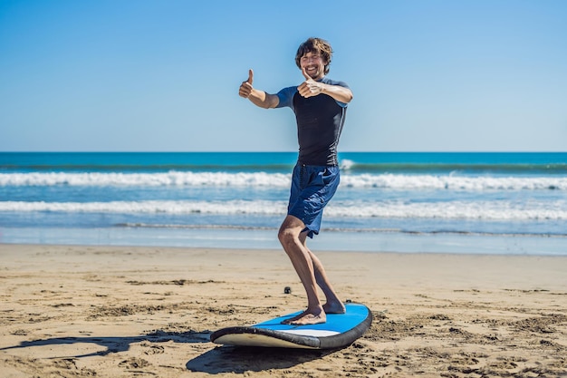 Młody człowiek szkolenia surfer przed pójściem do składu na piaszczystej plaży. Nauka surfowania. Koncepcja wakacji. Wakacje. Turystyka, sport