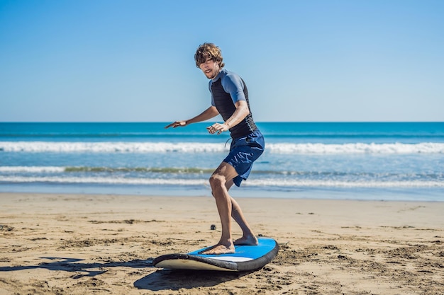 Młody człowiek szkolenia surfer przed pójściem do składu na piaszczystej plaży. Nauka surfowania. Koncepcja wakacji. Wakacje. Turystyka, sport