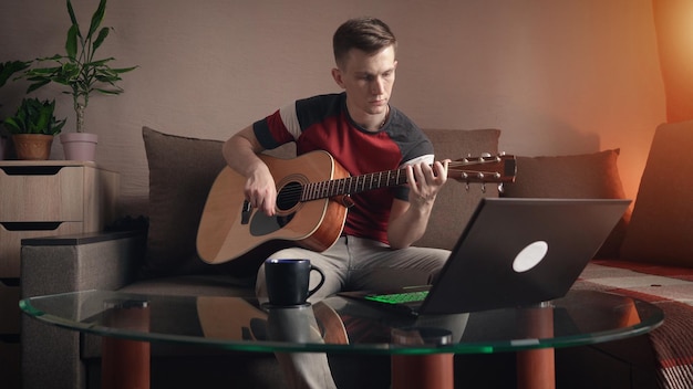 Młody człowiek uczy się grać na gitarze akustycznej online w domu