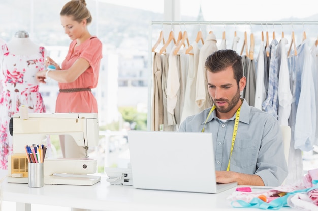Młody człowiek używa laptop z żeńskim projektantem mody pracuje w tle przy studiiem