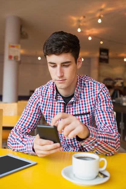 Młody człowiek używa telefon komórkowego w kawiarni