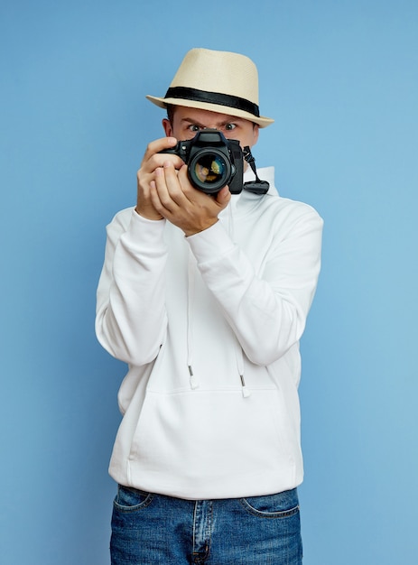 Młody człowiek w białym swetrze z kapeluszem i kamerą