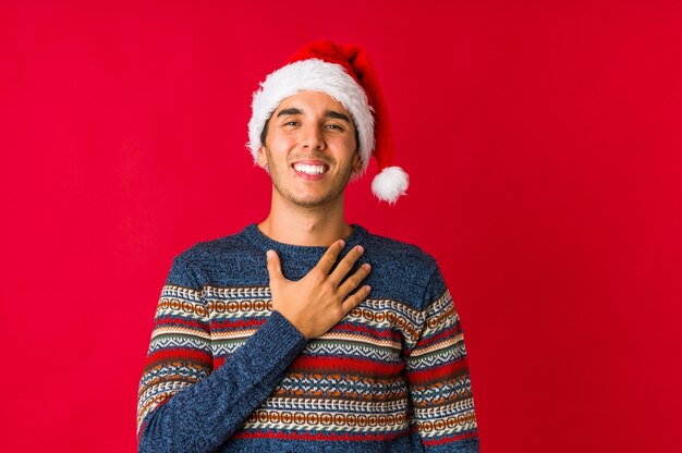 Młody człowiek w Boże Narodzenie trzyma ręce pod brodą, patrzy radośnie na bok.