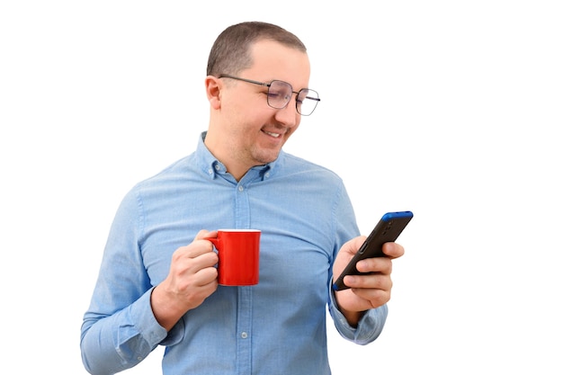 Młody człowiek w drelichowej koszuli mający gorący napój przy użyciu telefonu komórkowego na białym tle