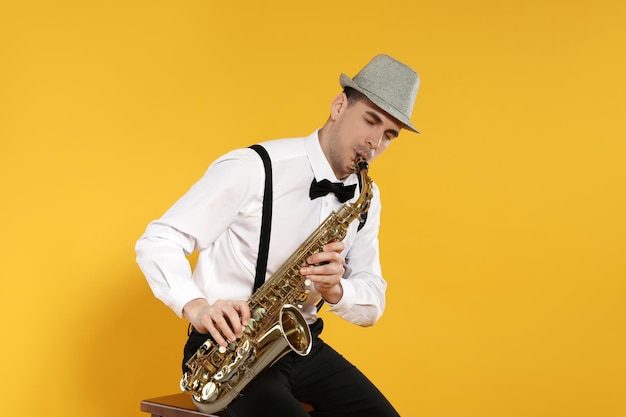 Młody człowiek w eleganckim stroju gra na saksofonie na żółtym tle