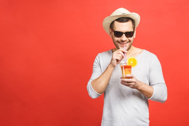 młody człowiek w kapelusz i okulary przeciwsłoneczne, stojąc i pijąc sok pomarańczowy