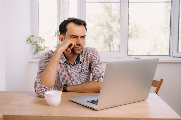 Młody człowiek w koszuli pracuje na laptopie w domu