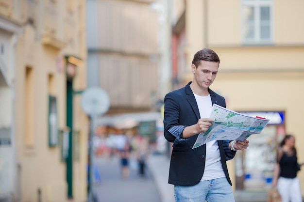 Młody człowiek w okularach przeciwsłonecznych z mapą miasta i plecakiem w Europie. Kaukaski turysta spoglądający na mapę europejskiego miasta w poszukiwaniu atrakcji.