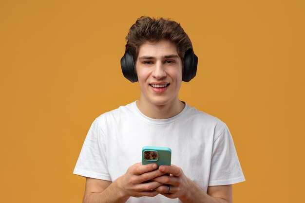 Młody człowiek w słuchawkach za pomocą telefonu komórkowego podczas słuchania muzyki na żółtym tle