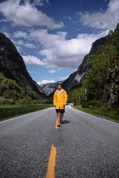Zdjęcie młody człowiek w żółtym płaszczu przeciwdeszczowym na drodze