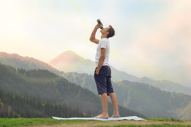 Młody człowiek wody pitnej na szczycie góry po praktyce jogi