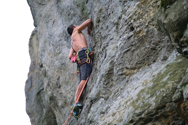 Młody człowiek wspinaczka stroma ściana skalistej góry. Wspinacz pokonuje trudną trasę. Angażowanie się w koncepcję sportów ekstremalnych.