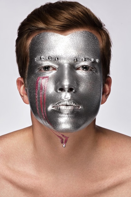 Młody człowiek z artystycznym makijażem artystycznym ze srebrną farbą na twarzy