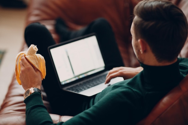 Młody Człowiek Z Bananem Pracuje Na Laptopie. Koncepcja Zarządzania Czasem.