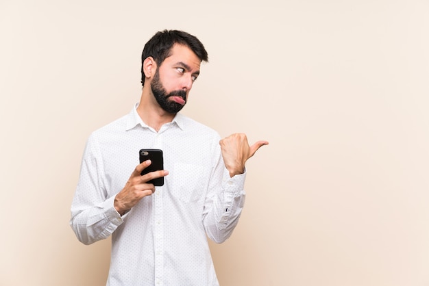 Młody człowiek z brodą, trzymając telefon niezadowolony i wskazując na bok