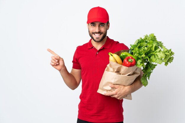 Młody człowiek z brodą, trzymając worek pełen warzyw na białym tle biały palec wskazujący z boku
