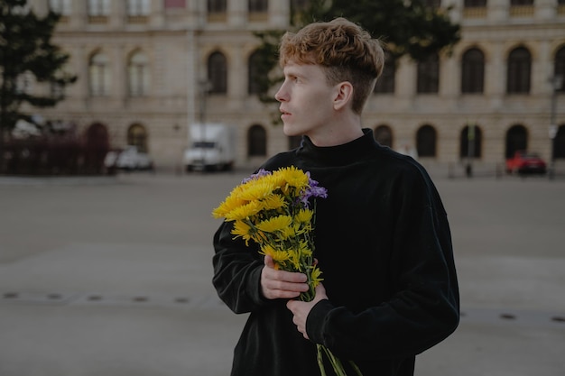 Młody człowiek z bukietem kwiatów odwraca wzrok w zamyśleniu