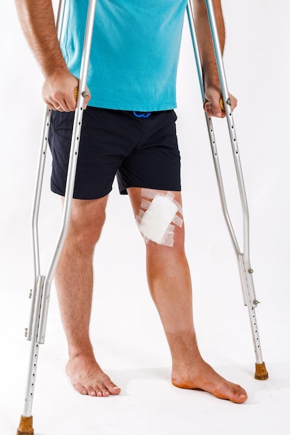 Młody człowiek z elastycznym bandażem na kolanie na białym tle mężczyzna na kulach chory kolano po operacji