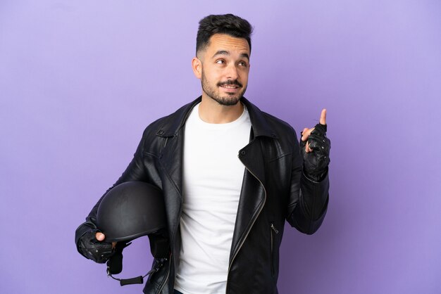 Młody człowiek z kaskiem motocyklowym na fioletowym tle wskazujący świetny pomysł