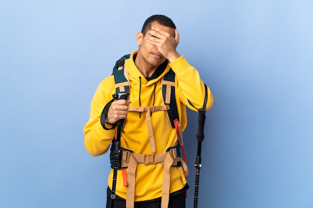 Młody człowiek z plecakiem i kijkami trekkingowymi na pojedyncze ściany zasłaniające oczy rękami