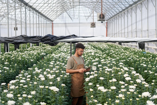 Młody człowiek z tabletką stojący wśród dużych kwiatów z chryzantemami