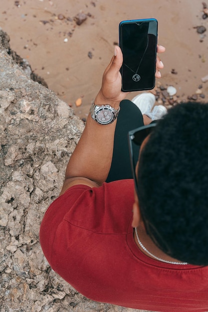 Młody człowiek z zegarkiem na nadgarstku wpatrujący się w telefon siedząc w parku