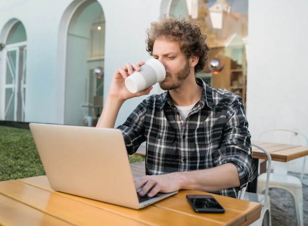 Młody człowiek za pomocą swojego laptopa w kawiarni