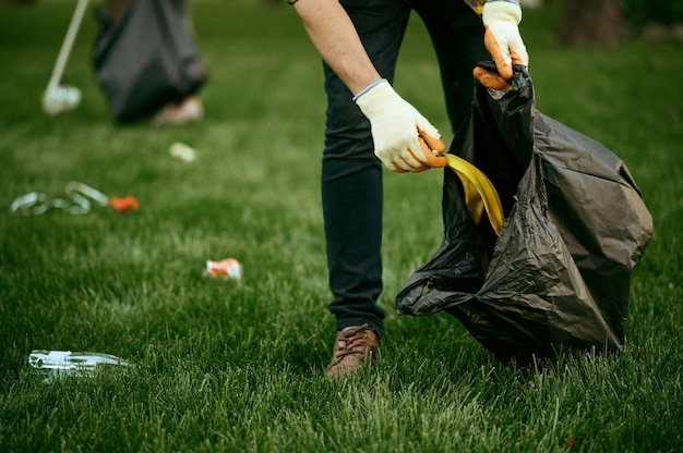 Młody człowiek zbiera śmieci w torbie w parku, dobrowolnie. Mężczyzna sprząta las, przywracanie ekologii, eko styl życia, zbiórka i recykling śmieci, opieka ekologiczna