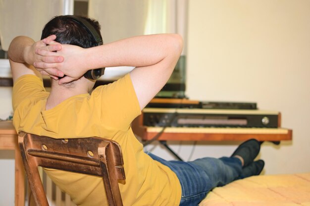 Zdjęcie młody człowiek zrelaksowany z rękami na karku, słuchając muzyki w słuchawkach