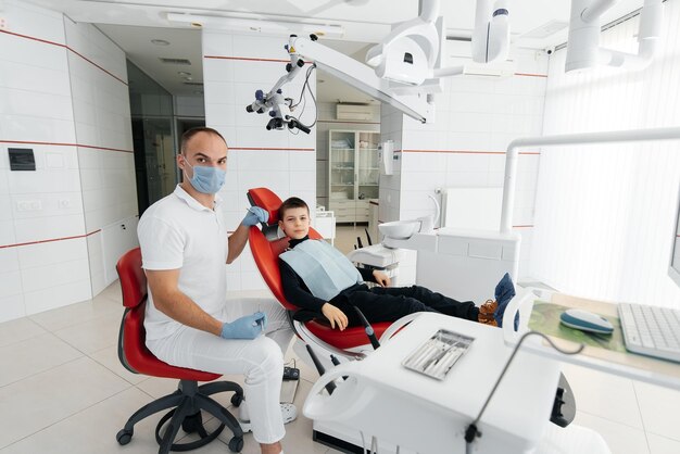 Młody dentysta bada i leczy zęby ośmioletniego chłopca w nowoczesnej białej stomatologii zbliżenie Leczenie protetyki stomatologicznej i wybielanie zębów Nowoczesna stomatologia Profilaktyka