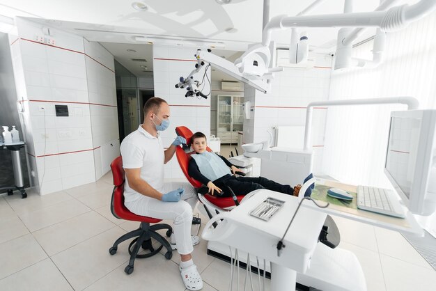 Młody dentysta bada i leczy zęby ośmioletniego chłopca w nowoczesnej białej stomatologii zbliżenie Leczenie protetyki stomatologicznej i wybielanie zębów Nowoczesna stomatologia Profilaktyka
