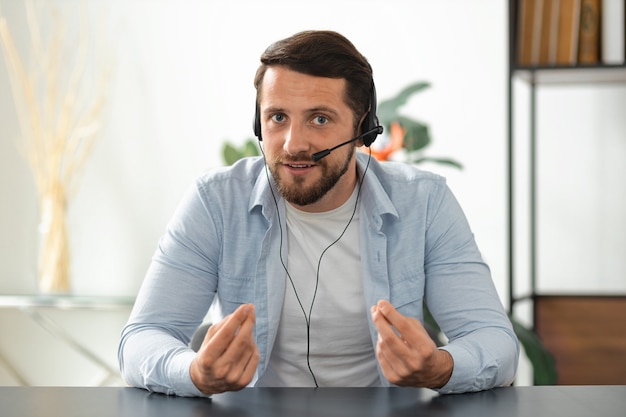 Młody Dorosły Człowiek Call Center Pracownika Lub Menedżera W Zestawie Słuchawkowym, Patrząc Na Kamery, O Spotkanie Biznesowe Online. Portret Portretowy Pracownika Odnoszącego Sukcesy, Który Komunikuje Się Ze Współpracownikami Za Pośrednictwem Rozmowy Wideo