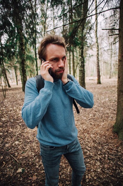 Młody dorosły mężczyzna rozmawia przez telefon stojący nad lasem zestresowany z ręką na głowie