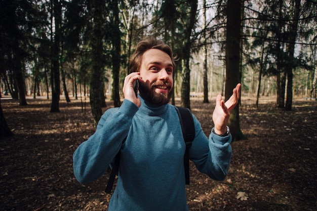 Młody dorosły mężczyzna rozmawia przez telefon stojący w lesie