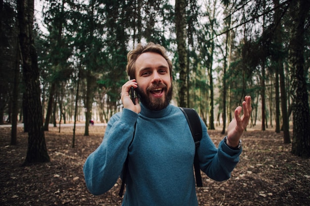 Młody dorosły mężczyzna rozmawia przez telefon stojący w lesie