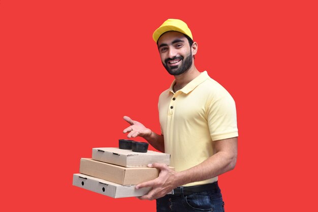 młody dostawca z przodu w żółtej koszulce i czapce, trzymający 3 pudełka po pizzy indyjski model pakistański