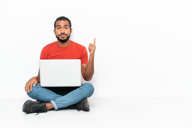 Młody Ekwadorczyk z laptopem siedzący na podłodze na białym tle wskazujący palcem wskazującym to świetny pomysł