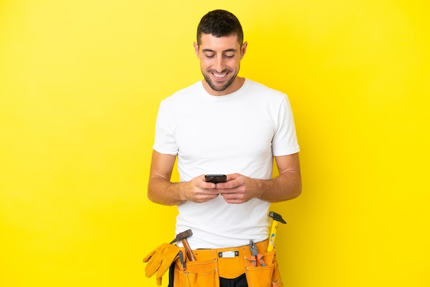 Młody elektryk kaukaski mężczyzna na białym tle na żółtym tle wysyłający wiadomość za pomocą telefonu komórkowego