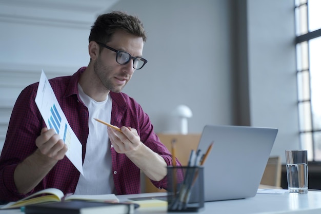 Młody europejski mężczyzna pracownik biurowy w okularach pokazujący raport statystyk podczas spotkania online