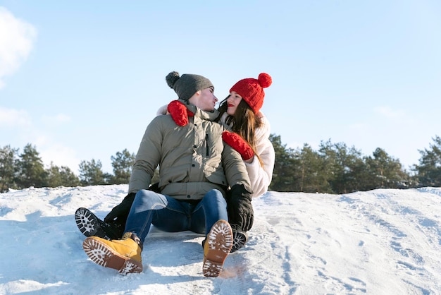 Młody facet i dziewczyna siedzą na śniegu na tle lasu i błękitnego nieba Para na zewnątrz
