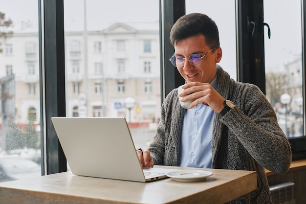 Młody facet jest freelancer w kawiarni działa za laptopem. człowiek pije kawę.