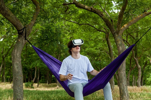 Zdjęcie młody facet siedzi w fioletowym hamaku nosząc okulary wirtualnej rzeczywistości wizualizacji 3d i bada przestrzeń rękami