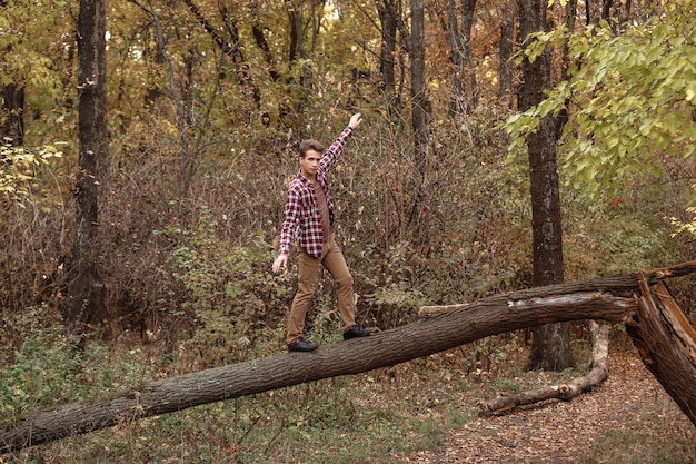 Młody facet w koszuli w kratę, chodzący po drzewie i bawiący się w lesie w jesienny dzień