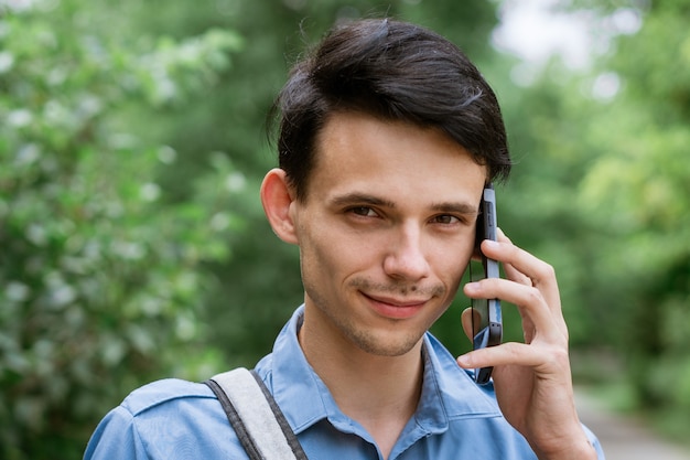 Młody facet w niebieskiej koszuli z plecakiem na ulicy na naturalne rozmowy przez telefon