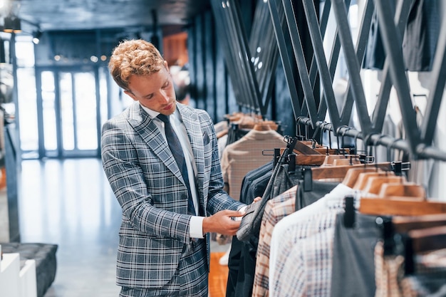 Młody facet w nowoczesnym sklepie z nowymi ubraniami Eleganckie drogie ubrania dla mężczyzn