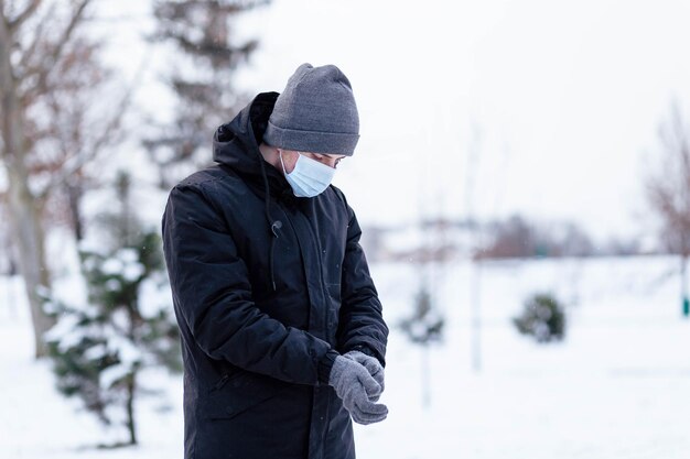 Młody facet w zimie nosi maskę Młody mężczyzna w ochronnej masce przeciwwirusowej na ulicy Facet w zimowym ubraniu w ochronnej masce Młody mężczyzna w ciepłych ubraniach i szaliku w zimowy dzień