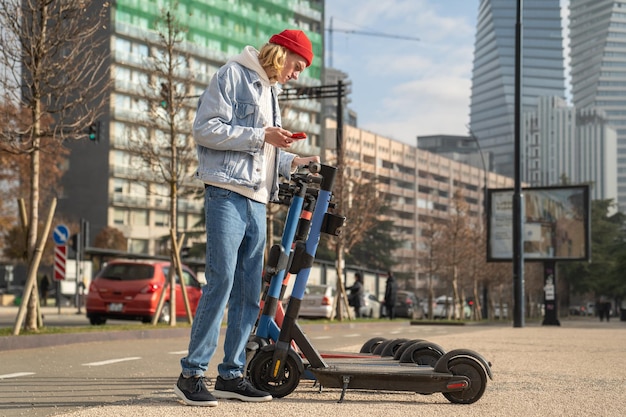 Młody facet wybiera elektryczny skuter do wynajęcia w mieście aktywujący się za pomocą smartfona koncepcja nowoczesnego miejskiego t