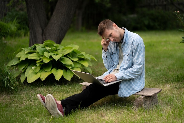 Młody facet wykonujący pracę zdalną na wakacjach, piszący na laptopie